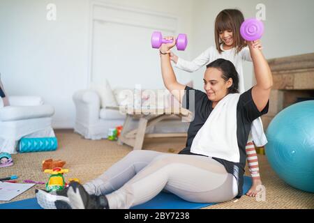 Tochter hilft Mutter trainieren mit Hanteln im Wohnzimmer Stockfoto