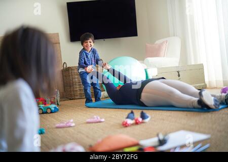 Junge spielt mit Mutter beim Training auf Yoga-Matte im Wohnzimmer Stockfoto