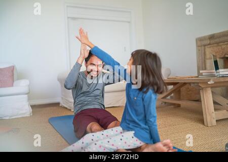 Glücklicher Vater und Tochter, die im Wohnzimmer auf einer Yogamatte fiving Stockfoto