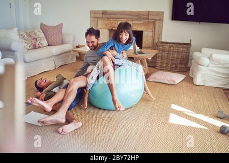 Verspielte Vater und Kinder auf Fitness-Ball im Wohnzimmer