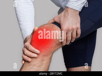 Knieverletzung oder Entzündung. Der Mann in Sportbekleidung drückt seine Hände auf das Knie, das rot hervorgehoben ist Stockfoto