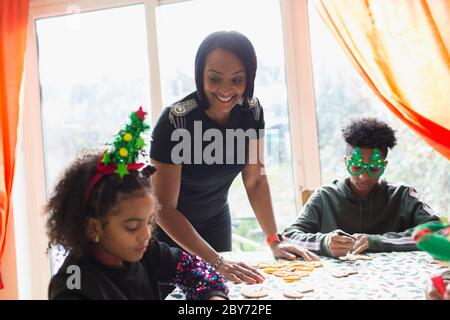 Glückliche Mutter und Kinder dekorieren Weihnachtskekse am Tisch Stockfoto