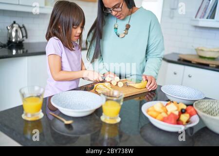 Mutter hilft Tochter schneiden Banane in der Küche Stockfoto