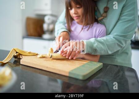 Mutter hilft Tochter schneiden Banane in der Küche Stockfoto