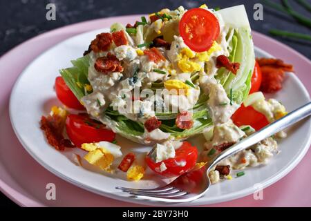 Nahaufnahme von Eisberg-Keil-Salat mit Blauschimmelkäse-Dressing, knusprig gebratenem Speck, Kirschtomaten, zerbröselten hartgekochten Eiern, Schnittlauch auf Tellern Stockfoto