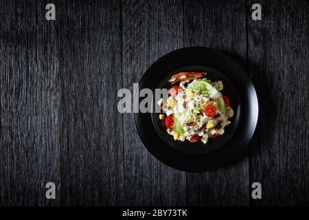 Eisberg-Keil-Salat mit Blauschimmelkäse-Dressing, knusprig gebratenem Speck, Kirschtomaten, zerbröselten hartgekochten Eiern, Schnittlauch auf schwarzen Tellern auf einem dunklen Stockfoto