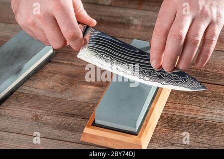 Mann, der ein Kochmesser mit einem nassen Stein schärft Stockfoto