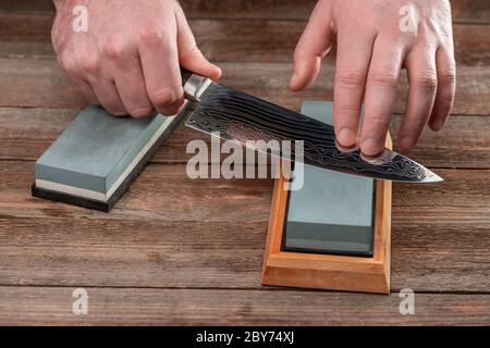 Mann, der ein japanisches Messer mit einem Wetzstein schärft Stockfoto