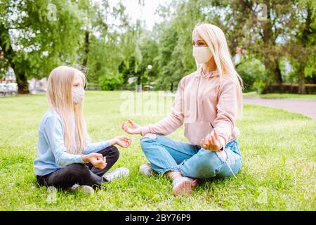 Mutter und kleine Tochter im Park mit Schutzmasken. Mama lehrt Mädchen Yoga. Familie, Muttertag, kovidische Pandemie Stockfoto