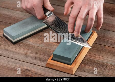 Mann schärft ein japanisches Kochmesser mit einem nassen Wetzstein Stockfoto