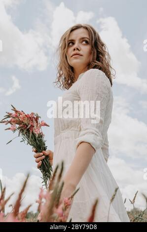 Low-Winkel Nahaufnahme Porträt von jungen Frau in weiß gekleidet und hält Blumen auf der Seite Stockfoto