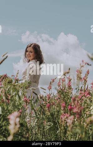 Low-Winkel-Seitenansicht Porträt einer jungen Frau in weißem Kleid lächelt an der Kamera in einem blühenden Blumenfeld Stockfoto