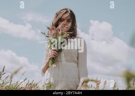 Obere Seite Vorderansicht Porträt der jungen Frau in langen weißen Kleid hält einen Blumenstrauß auf das Gesicht Stockfoto