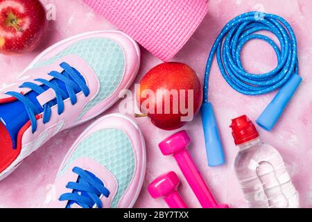 Yogamatte, Sportschuhe, Springseil, Hanteln, Apfel, Flasche Wasser auf rosa Hintergrund. Konzept gesunde Lebensweise, gesunde Ernährung, Sport und Ernährung. Sp Stockfoto