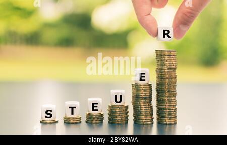 Würfel bilden das deutsche Wort "Steuer" auf immer höhere Münzstapel. Stockfoto