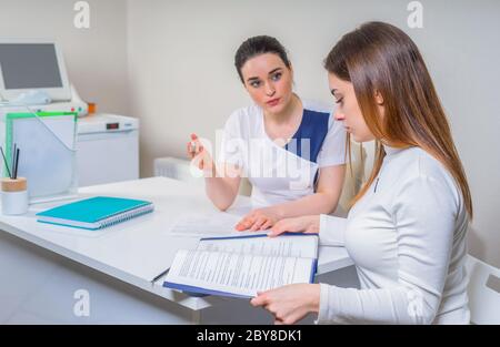 Junge Ärztin sitzt an ihrem Schreibtisch und plaudert mit der Patientin, während sie ihre Testergebnisse zeigt Stockfoto