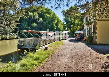 Carcassonne Aude Frankreich 07/11/19 Canal du Midi Schleppweg und Schleusenwärterhütte. Kanalrundfahrt Boot neben einem Café. Urlauber genießen eine kühle Stockfoto