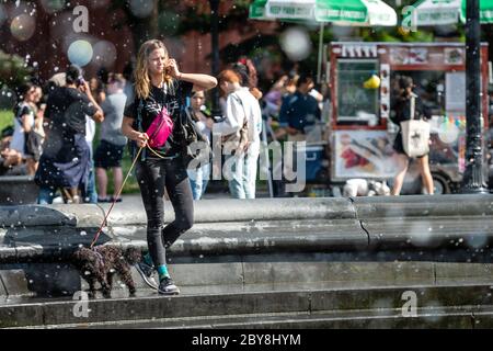 New York, USA - 21. Juni 2019: Durch Brunnen Tropfen können gesehen werden, wie eine Frau mit einem Hund spazieren und spricht über das Telefon. Stockfoto