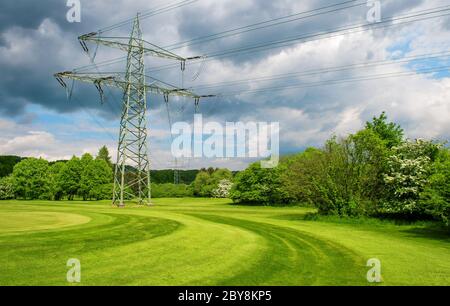 Hochspannungsleitungen und Strommasten. Naturlandschaft Golfplatz und wolkig blauer Himmel Stockfoto