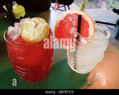 Zwei schöne frische Fruchtgetränke für Sommeraperitif in Glasgläsern und verschiedene Garnituren auf einem Tisch Stockfoto