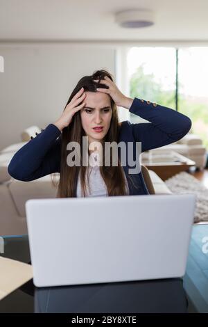 Besorgte junge Frau vor dem Laptop im Wohnzimmer. Fail und Technologiekonzept. Stockfoto