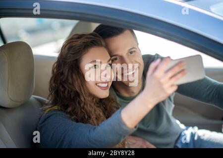 Junges Paar sitzt im Auto, macht Selfie und lächelt Stockfoto