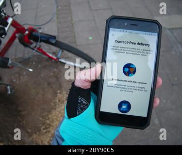 Deliveroo Cycle Kurier Food Delivery Rider überprüft kontaktlose Lieferführung auf Telefon-App. Stockfoto