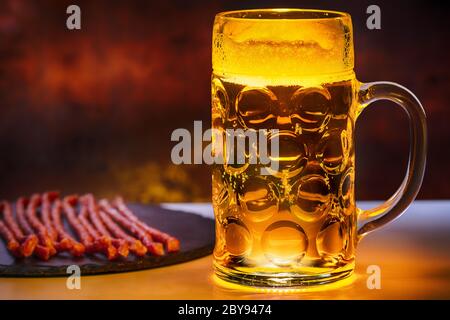 TANKARD mit eiskaltem Bier und getrockneten würzigen Wurstsnacks auf einer Platte in einem Pub in einem Nahaufnahme von der Seite Stockfoto