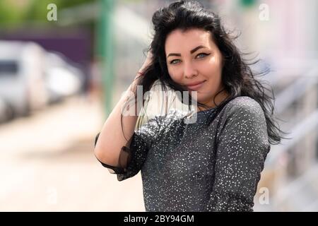 Attraktive Frau mit ihren langen Haaren weht in der Brise und lächelt an der Kamera im Freien auf einem Parkplatz in Nahaufnahme Stockfoto