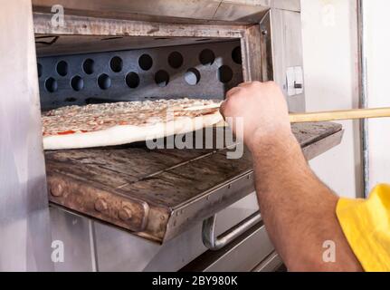 Pizza und Pizzaherstellung - Hand legen Pizzakuchen in Ofen auf einer hölzernen Pizzaschale Stockfoto