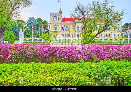 BANGKOK, THAILAND - 13. MAI 2019: Die Fassade des Thai-Khu-Fah Palast des Regierungshauses durch das üppige Grün und Bougainvillea Blumen rund um die Stockfoto