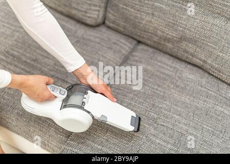 Frau saugen Möbel in einem Haus mit einem tragbaren Handstaubsauger. Stockfoto