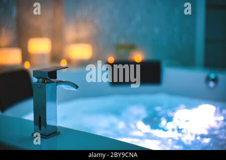 Blaues sprudelndes Wasser im Spa Jacuzzi Close-up Wasserhahn mit Kerzen auf dem Hintergrund, entspannen und Lifestyle Abstrakten Hintergrund mit blauen Lichtern dekoriert Stockfoto