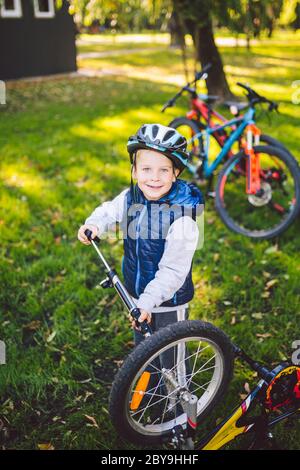 Kaukasischer Junge in einem Helm lernt, sein Fahrrad zu reparieren. Der Fahrradfahrer überprüft den Mechanismus eines Fahrrads in einer grünen Wiese im Park Stockfoto