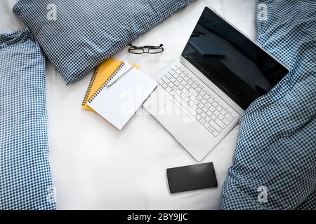 WFH - Arbeit von zu Hause Laptop, Notizblock und Handy auf Bett 1 Stockfoto