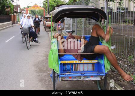 JOGJAKARTA, INDONESIEN - 12. JUNI 2013: Rikscha-Fahrer schläft auf der Arbeit in den Straßen von Yogyakarta, Indonesien. Weil Taxi mit Fahrer Person Schlitten Stockfoto