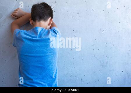 Verärgert trauriger Junge stehen allein zurück und lehnen sich an die Wand. Lernschwierigkeiten, familiäre Probleme, Mobbing, Depression, Stress oder Frustration Konzept Stockfoto