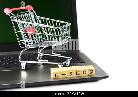 E - Shop gefaltet mit Würfeln mit Buchstaben auf dem Hintergrund eines Laptops und Trolley 2 Stockfoto