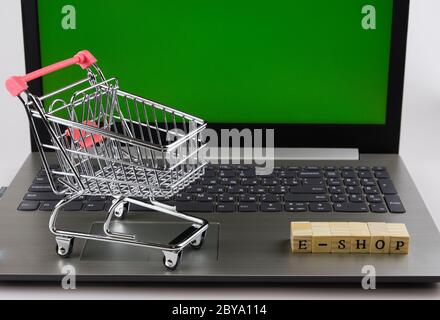 E - Shop gefaltet mit Würfeln mit Buchstaben auf dem Hintergrund eines Laptops und Trolley 3 Stockfoto