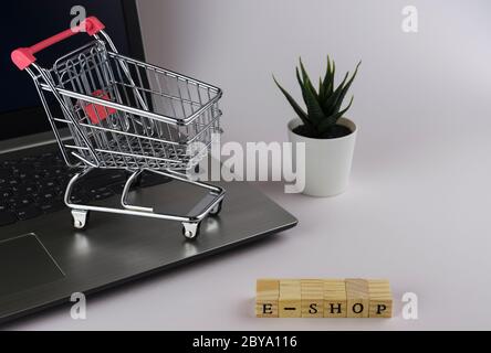E - Shop gefaltet mit Würfeln mit Buchstaben auf dem Hintergrund eines Laptops und Trolley 4 Stockfoto