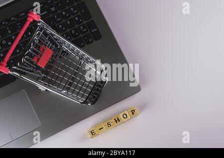 E - Shop gefaltet mit Würfeln mit Buchstaben auf dem Hintergrund eines Laptops und Trolley Stockfoto