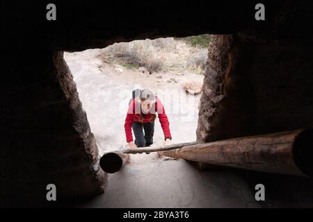 NM00621-00...NEW MEXICO - Klettern eine Leiter zu Klippenwohnungen, Talushäuser, entlang der Main Loop Trail in Bandelier National Monument. Stockfoto