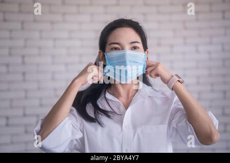 Schöne junge asiatische Frau trägt Gesichtsmaske covid19 Virus gegen weiße Ziegelwand zu schützen Stockfoto