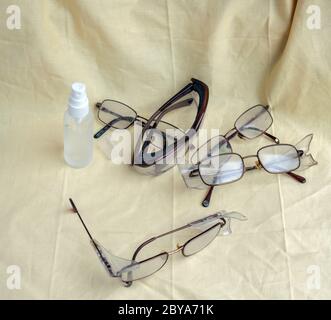 Eine Draufsicht auf verschiedene Paare von Gläsern und Schutzbrillen zusammen mit einer Sprühflasche Glasreiniger. Stockfoto