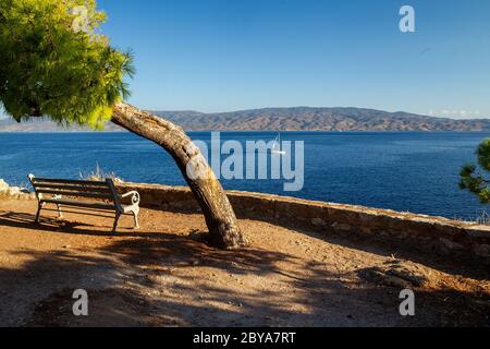 Bank für die Beobachtung des Meeres und Schiffe Segeln und Festland Griechenland in schönen sonnigen Sommertag im Schatten der Kiefer - Baum auf erstaunliche Insel Hydra Stockfoto