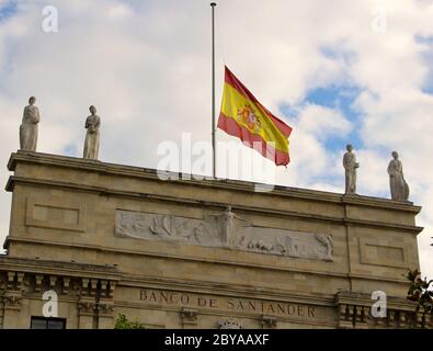 Ursprüngliches Hauptgebäude der Santander Bank (Banco de Santander) spanische Nationalflagge am Halbmast aus der Nähe von den Pereda-Gärten in Spanien Stockfoto