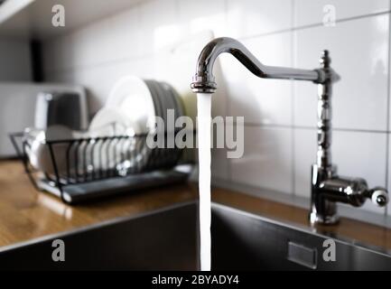 Wasser fließt aus einem Küchenhahn aus Edelstahl in das Waschbecken. Verschwenden von Wasser, indem Sie einen Chrom-Wasserhahn laufen lassen. Wassermissbrauch im Haushalt Stockfoto