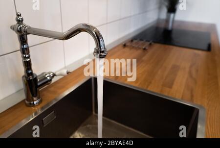 Wasser fließt aus einem Küchenhahn aus Edelstahl in das Waschbecken. Wassermissbrauch bei häuslichen Pflichten und Tätigkeiten. Zu viel Haushaltswasser. Verschwendung Stockfoto