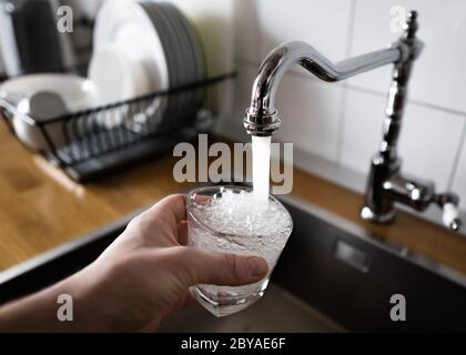 Männliche Hand Gießen Wasser in das Glas aus Chrom Wasserhahn fließendes Wasser mit Luftblasen zu trinken. Trinkwasser und sicher zu trinken. Mann Füllen ein Stockfoto