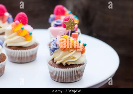 Schokoladencupcakes mit Frischkäse-Zuckerguss, pinka und Orangenkauen-Marmelade, Süßigkeiten und goldenem Topper auf dunklem Hintergrund Stockfoto